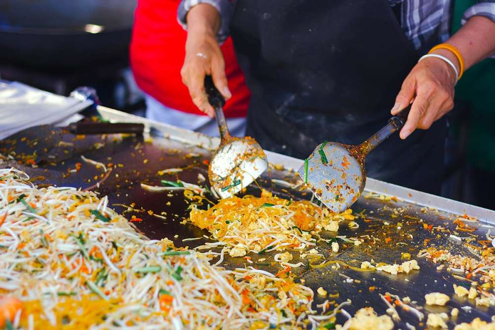 Mulher preparando comida em uma barraca na Khao San Road, Tailândia, à noite